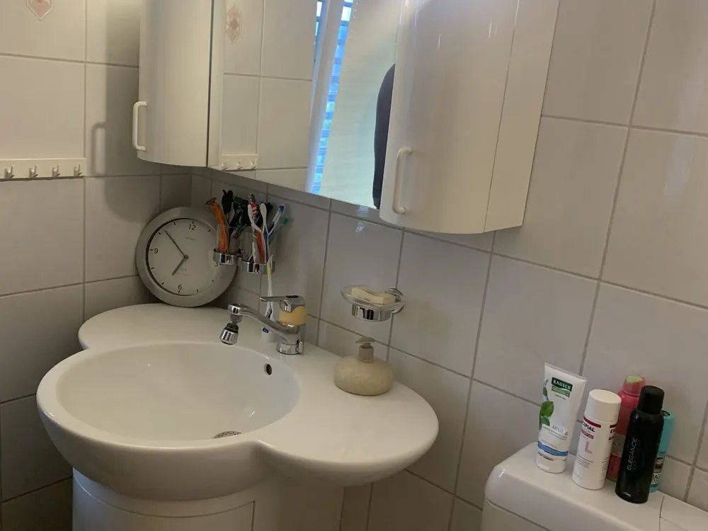 Bad vor der Sanierung: weisses Lavabo, weisse Wandfliesen und Spiegelschrank