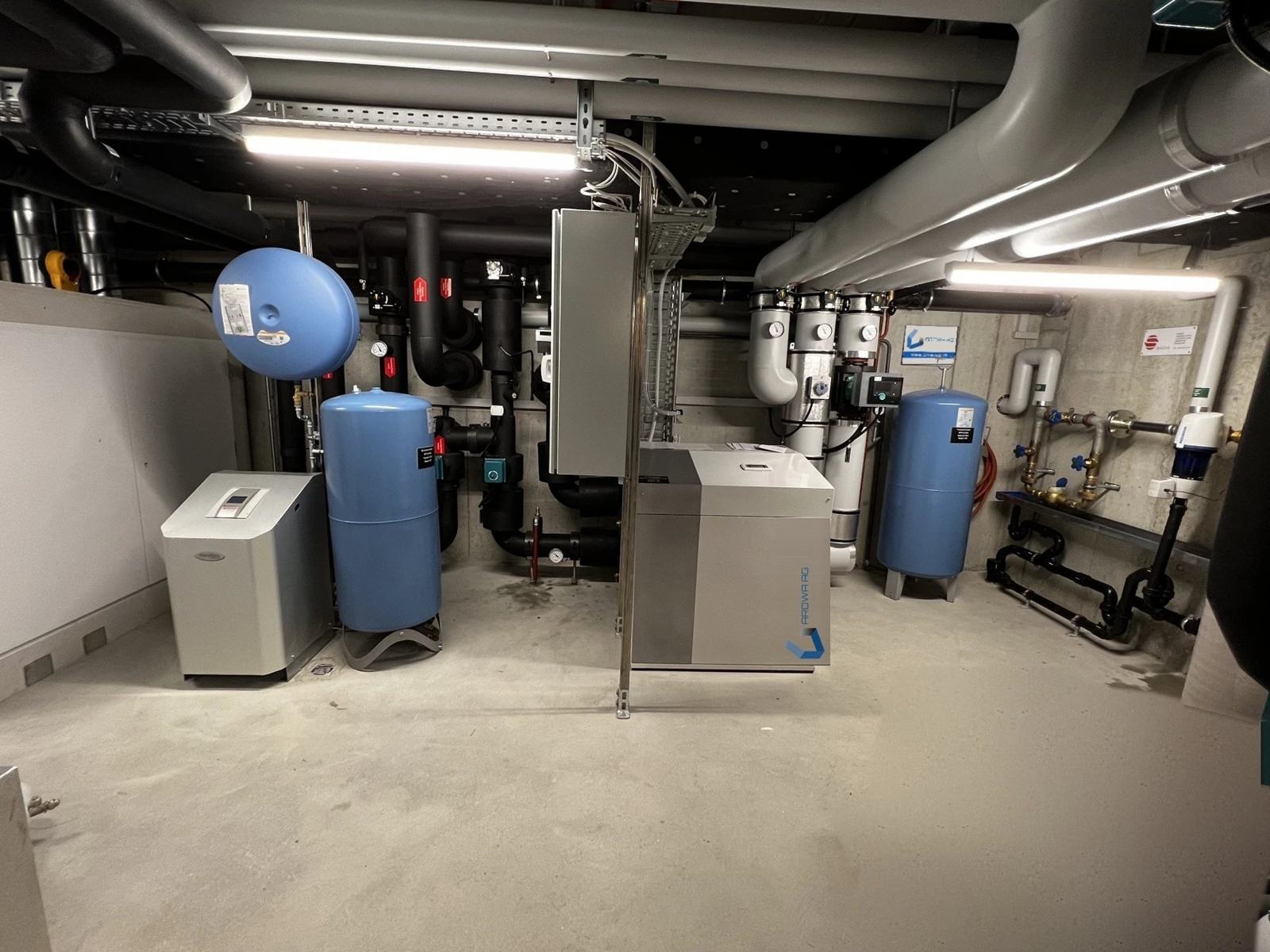Technikraum in Ebmatingen mit Wärmepumpe, blauen Ausdehnungsgefässen und isolierten Leitungen